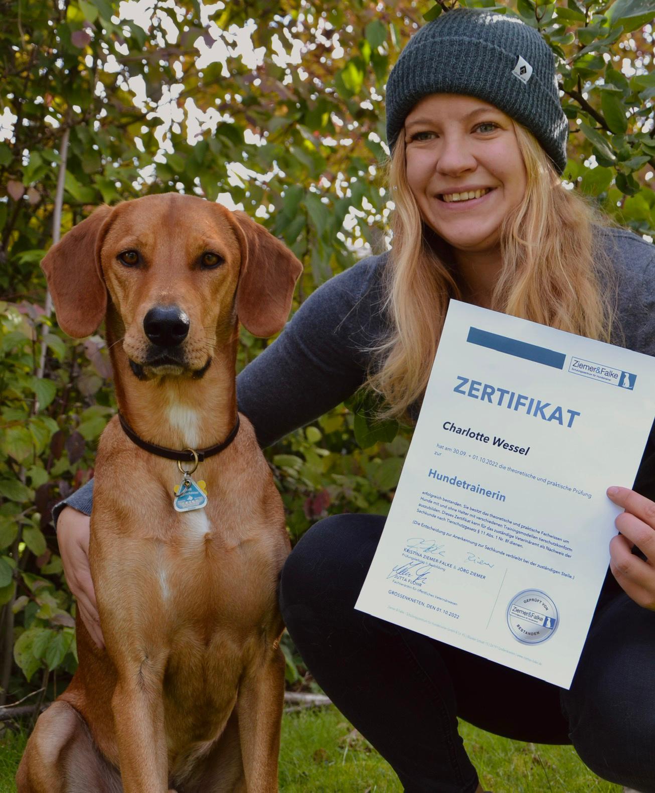 Charlotte mit ihrem Hund und in ihrer Hand hält sie das Zertifikat zur Hundetrainerin